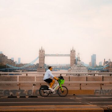 Man rides bicycle across bridge with london skyline.