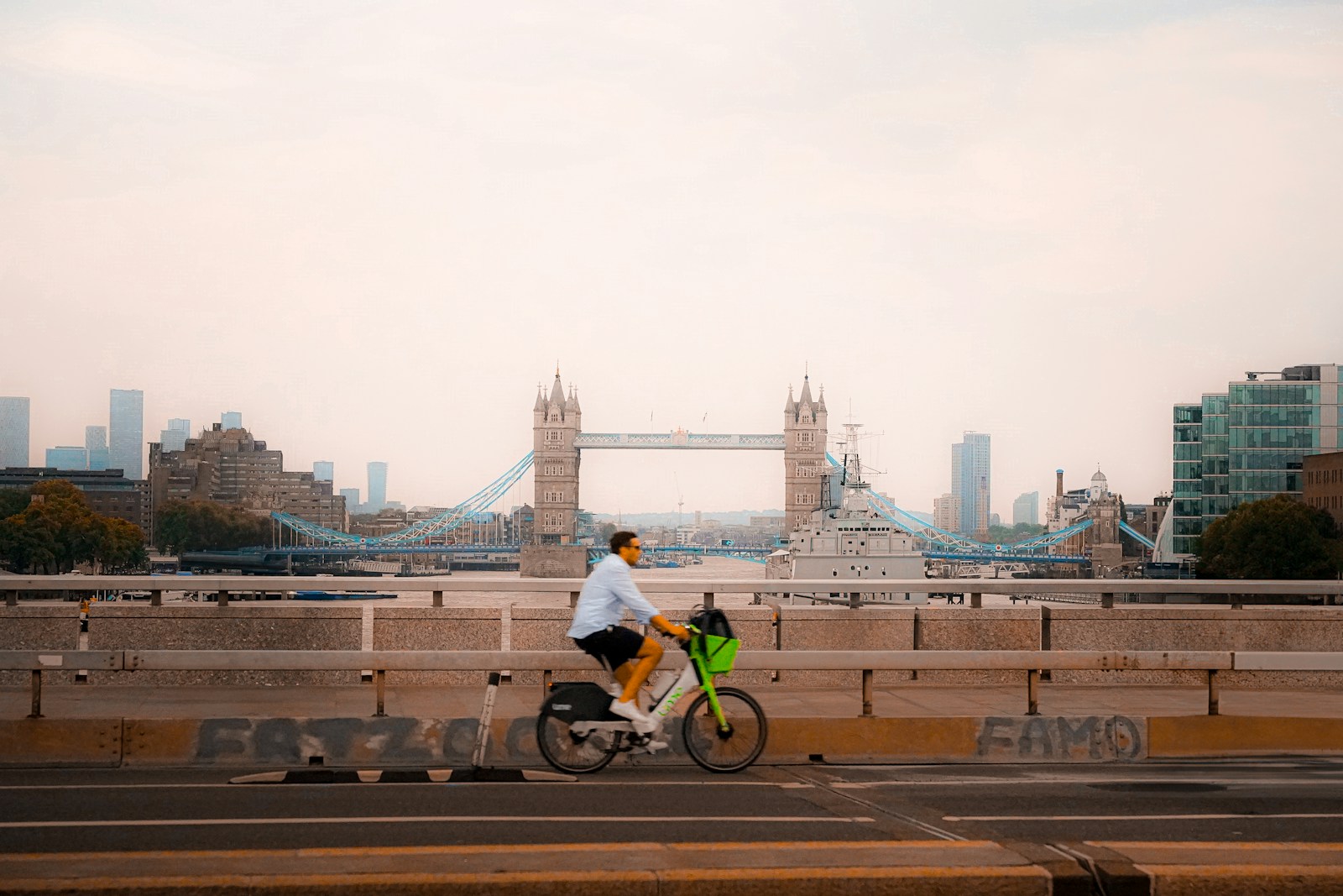 Man rides bicycle across bridge with london skyline.